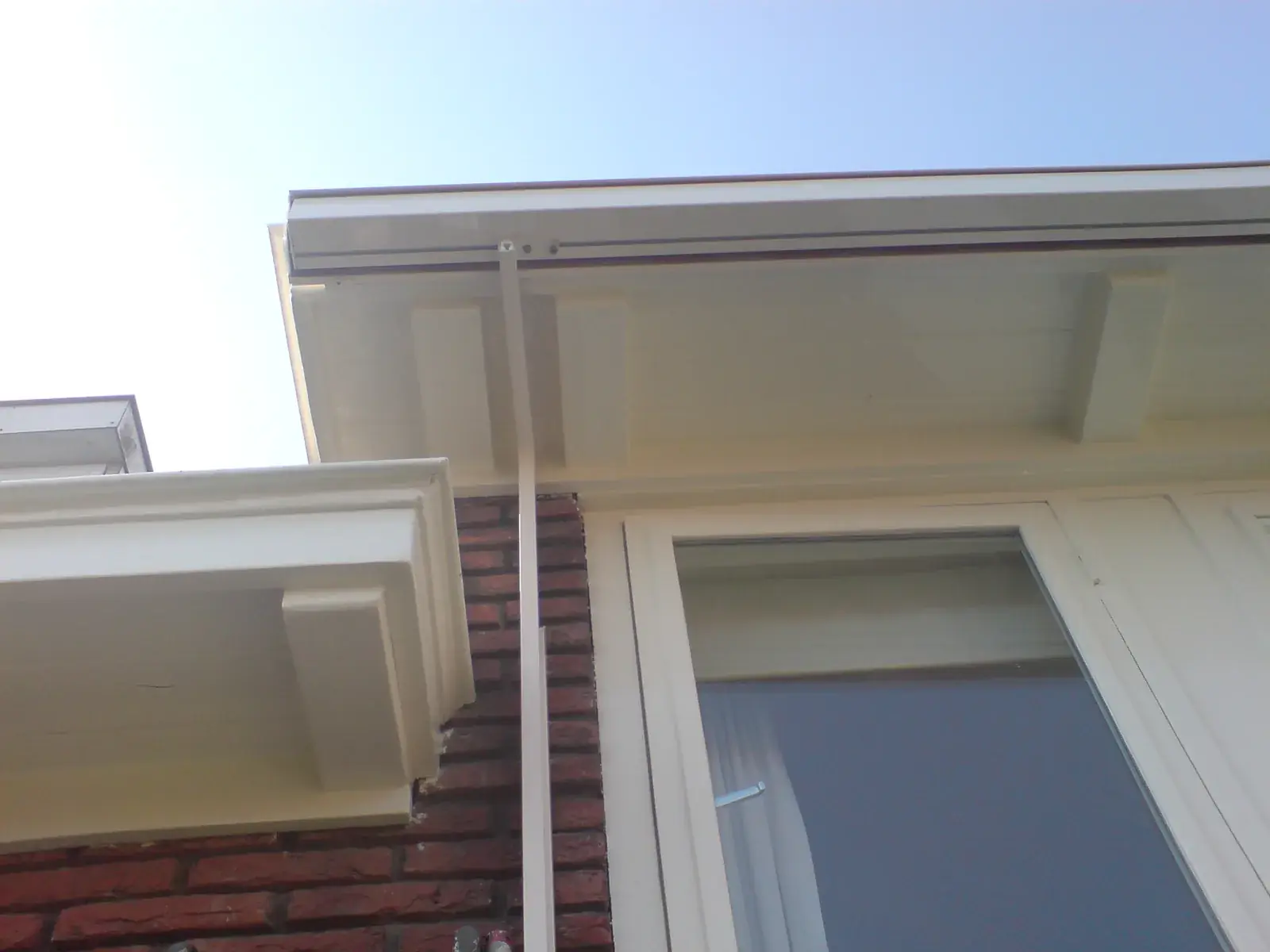 Cr&egrave;mekleurig uitvalscherm met steunarm onder het overstek van een dakkapel, afgestemd op het kozijnwerk