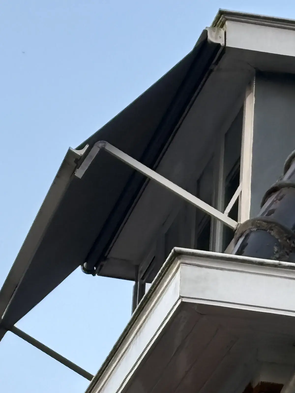 Uitvalscherm met balkonhoekarm volledig uitgevouwen voor het raam van een dakkapel met overstek