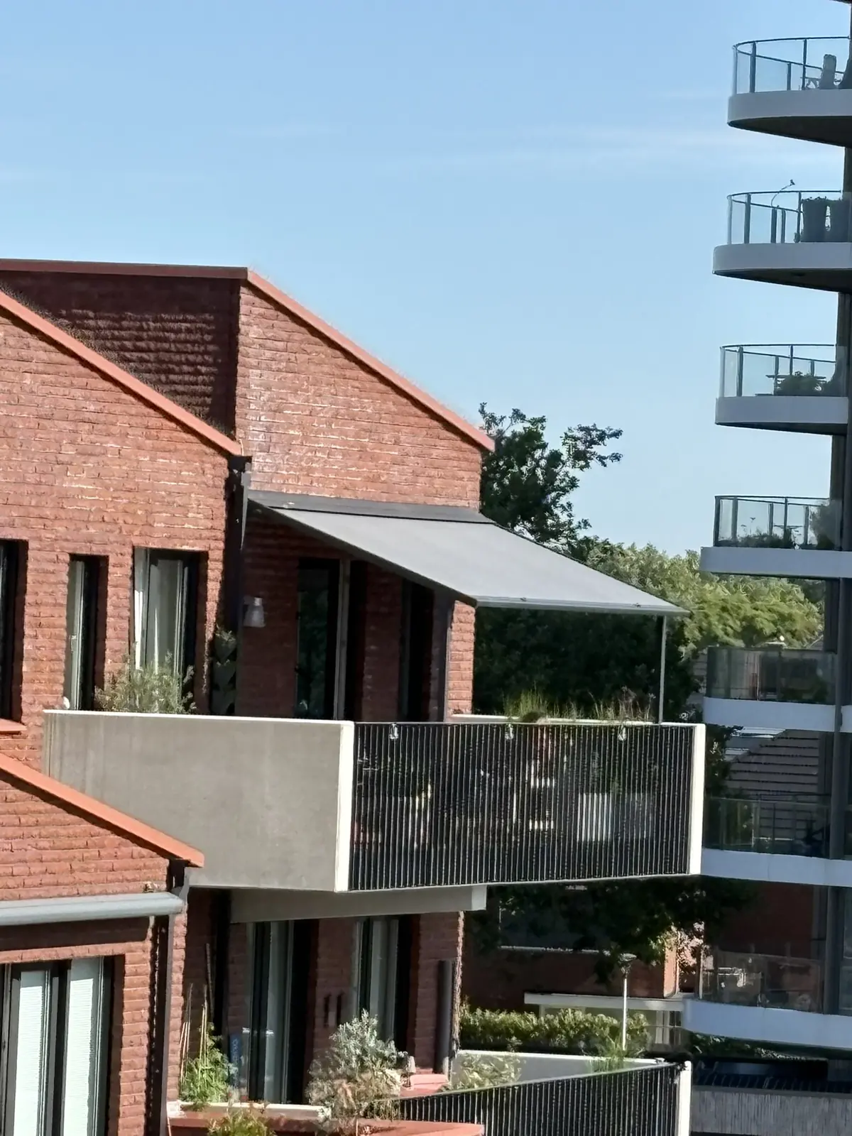 Antracietgrijze cassette van een knikarmscherm tegen de rode bakstenen gevel van Waterpark