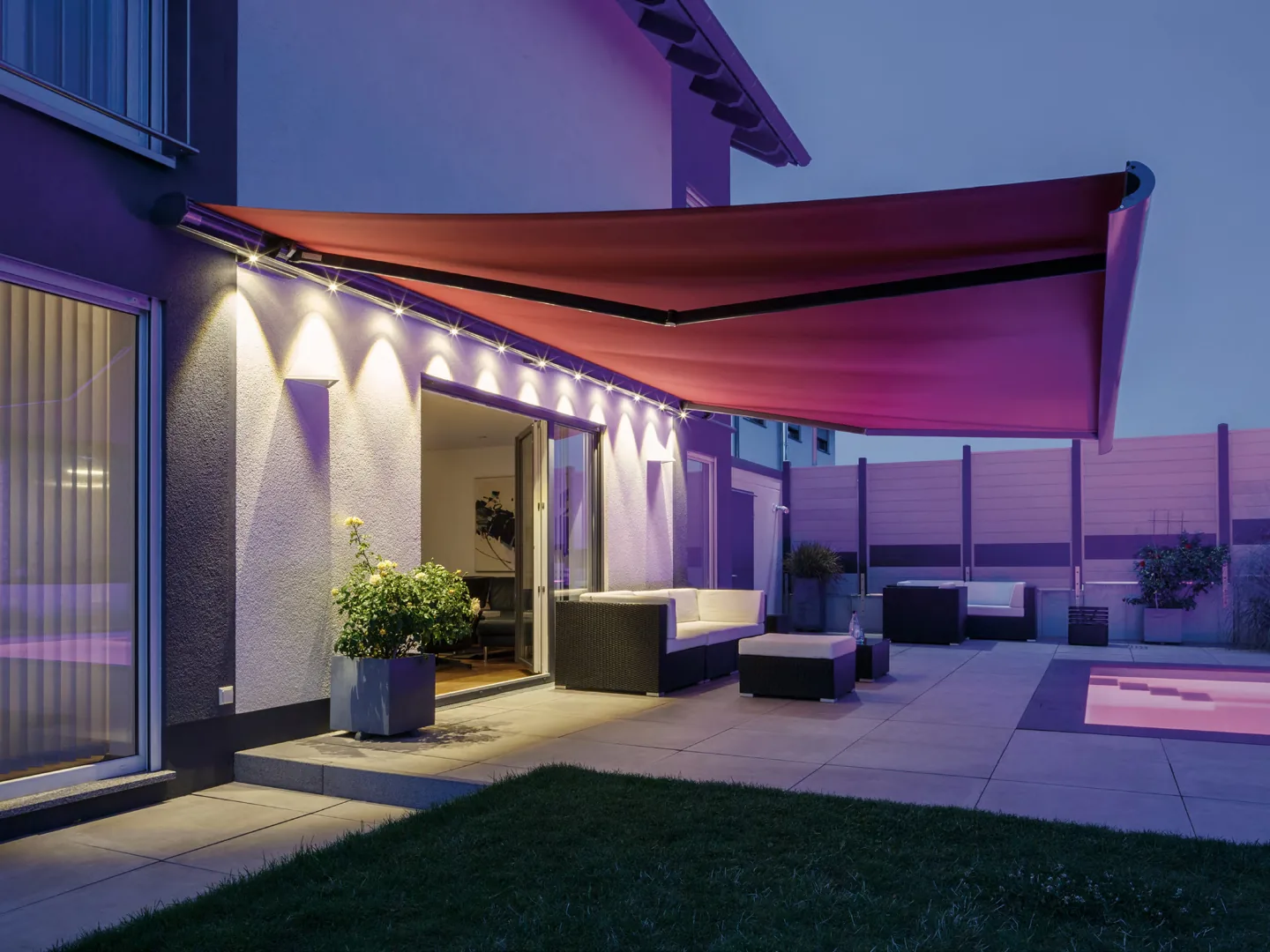 Weinor Opal Design II knikarmscherm met rood doek en led-verlichting boven een terras in de avond